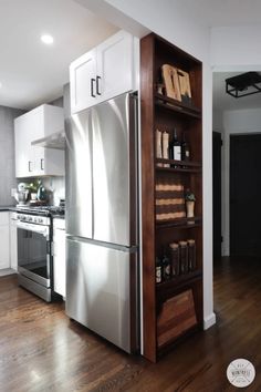 a stainless steel refrigerator in a kitchen with white cabinets and wood flooring next to an open shelving unit