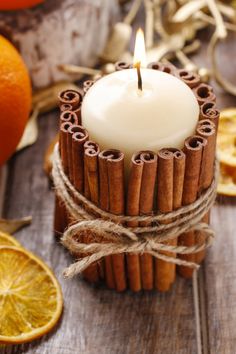 cinnamon sticks are wrapped around a candle on a wooden table next to oranges and an orange slice