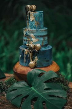 a three tiered blue cake with gold decorations sits on top of a wooden table