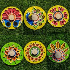 four colorful painted plates sitting on top of a green grass covered field next to a candle holder