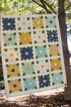 a quilt hanging from a tree in the woods with blue, yellow and green flowers on it