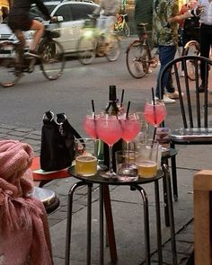 two tables with drinks on them in the middle of a busy city street while people walk by