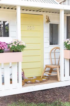 a porch with flowers and a rocking chair on the front steps, next to a yellow door