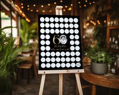 an easel with a sign on it in front of a table and potted plants