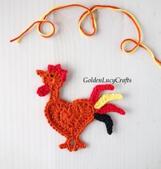 a crocheted rooster ornament hanging from a string on a white surface