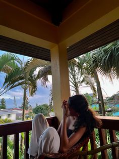 a woman sitting in a chair on top of a wooden porch next to palm trees