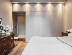 a bedroom with white bedding and wooden dresser next to a wall mounted light fixture