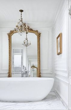 a large white bathtub sitting under a mirror in a bathroom next to a chandelier