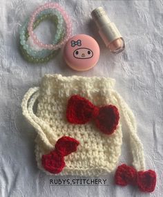 a crocheted purse with red bows and other items on it sitting on a white sheet