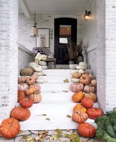 pumpkins and gourds are arranged on the front steps of a white brick house