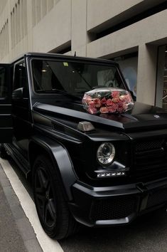 a black car with flowers on the hood parked in front of a building