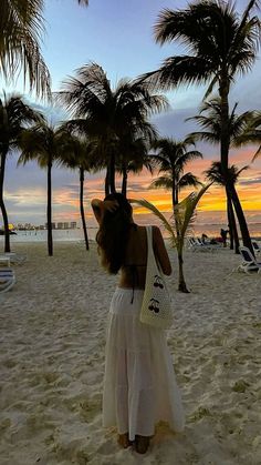 a woman standing on top of a sandy beach next to palm trees and the ocean