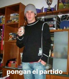 a man standing in front of a book shelf holding a drink and looking at the camera