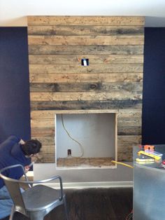 a man working on a fireplace in a room with blue walls and wood paneling