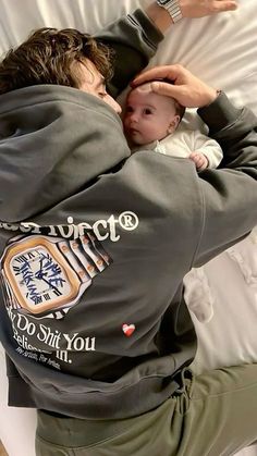 a man holding a baby in his arms while laying on top of a bed next to pillows