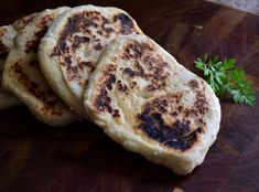 three flat breads sitting on top of a wooden cutting board next to a parsley