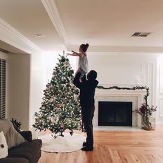 a man and woman are decorating a christmas tree in the living room with a fireplace