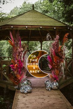 the entrance to the outdoor wedding venue is decorated with feathers and metal balls, as well as an illuminated sign that reads to the moon back