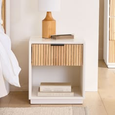 a nightstand with books and a lamp on it in a white room next to a bed