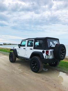 a white jeep parked on top of a dirt road next to the ocean and grass