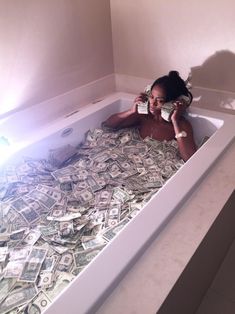 a woman in a bathtub full of money talking on the phone and drinking water