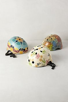 three colorful helmets sitting next to each other on a white surface, one with flowers and leaves painted on it