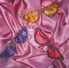 three pairs of sunglasses laying on a pink satin surface with beads and sequins