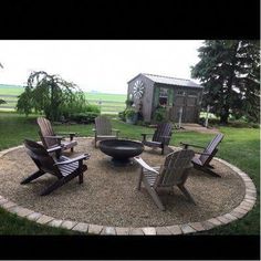 a fire pit surrounded by lawn chairs in the middle of a yard with an out building behind it