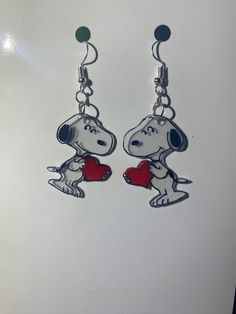 a pair of earrings with a cartoon dog holding a heart in it's paws