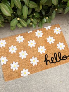 a door mat with the word hello written on it next to some flowers and leaves