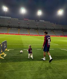 a man standing next to a little boy on top of a soccer field at night