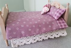 a wooden doll bed with pink and white bedspread on it's sides