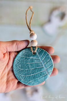 a hand holding a stone with a leaf on it and two beads hanging from it