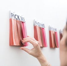 a woman is pointing to some pink and red strips on a wall with the words pick me