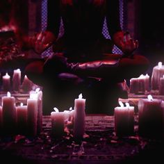 a person sitting in a meditation position surrounded by lit candles with their hands on the ground