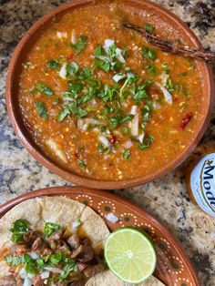 two bowls of soup with tortillas, lime and cilantro on the side