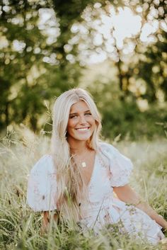 a woman sitting in tall grass smiling for the camera with her long blonde hair blowing back