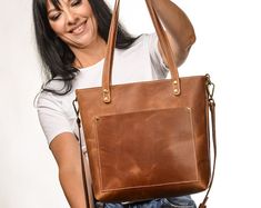 a woman holding onto a brown leather handbag and smiling at the camera with her right arm in the air