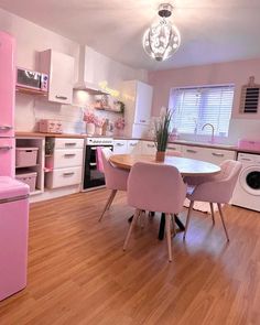 a pink refrigerator and table in a small room with hardwood floors, white cabinets and appliances