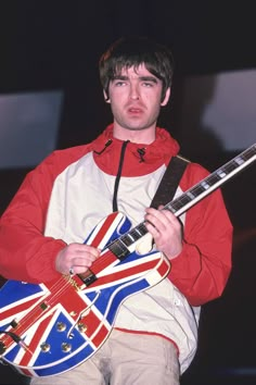 a man holding a guitar in his right hand and wearing an union jack outfit on the other