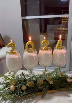 four glasses filled with white liquid and gold numbers on top of a table in front of a window