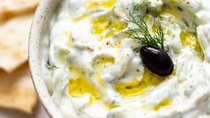 an image of a bowl of dip with olives and crackers on the side