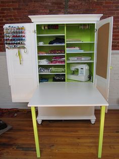 a white desk with green shelves in front of a brick wall and wooden flooring