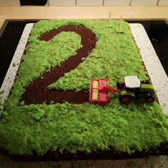 there is a tractor on top of the number two cake that has grass growing out of it