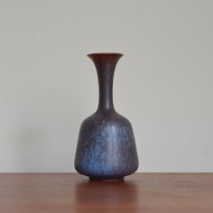 a brown vase sitting on top of a wooden table next to a white wall in the background