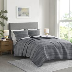 a bed in a bedroom with a gray and white comforter set on top of it