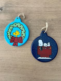 two ornament shaped like cartoon characters hanging from strings on a wooden table top