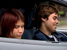 a young man and woman sitting in the back seat of a car looking at each other