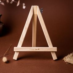 a small wooden easel sitting on top of a brown table next to a plant