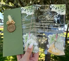 a person holding up a green and white wedding card with a gold brooch on it